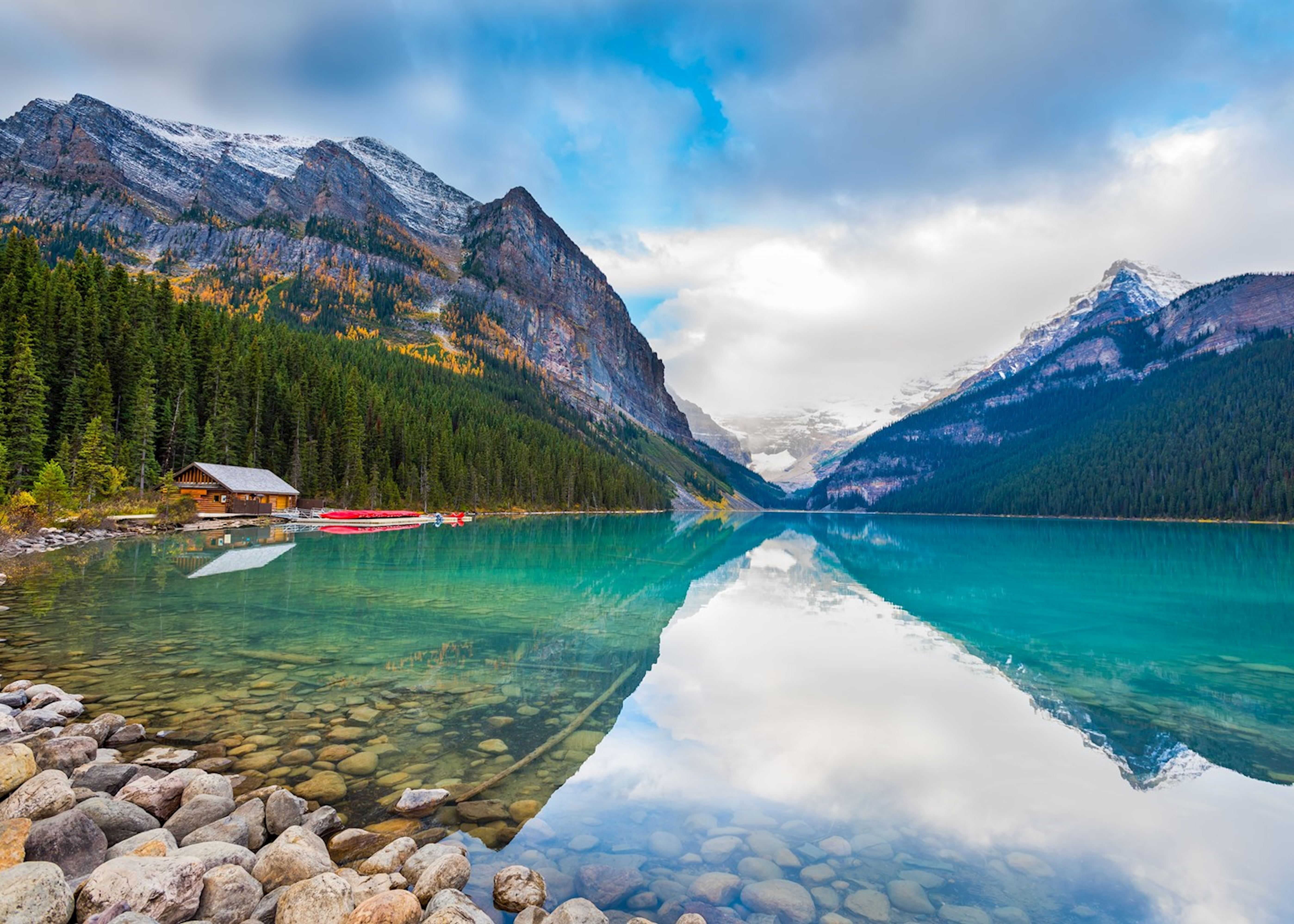 Lake Louise in Banff National Park with turquoise water, mountain reflections, forest shoreline and a lakeside cabin in Alberta, Canada.
