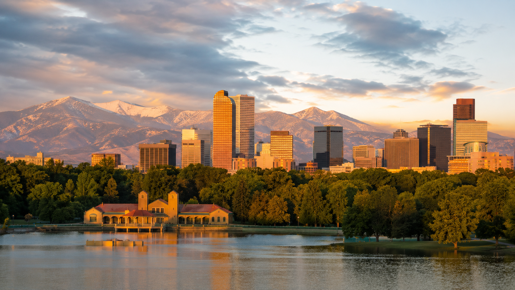 Denver skyline at golden hour with city high-rises, mountain backdrop, lake reflections and City Park in Colorado.