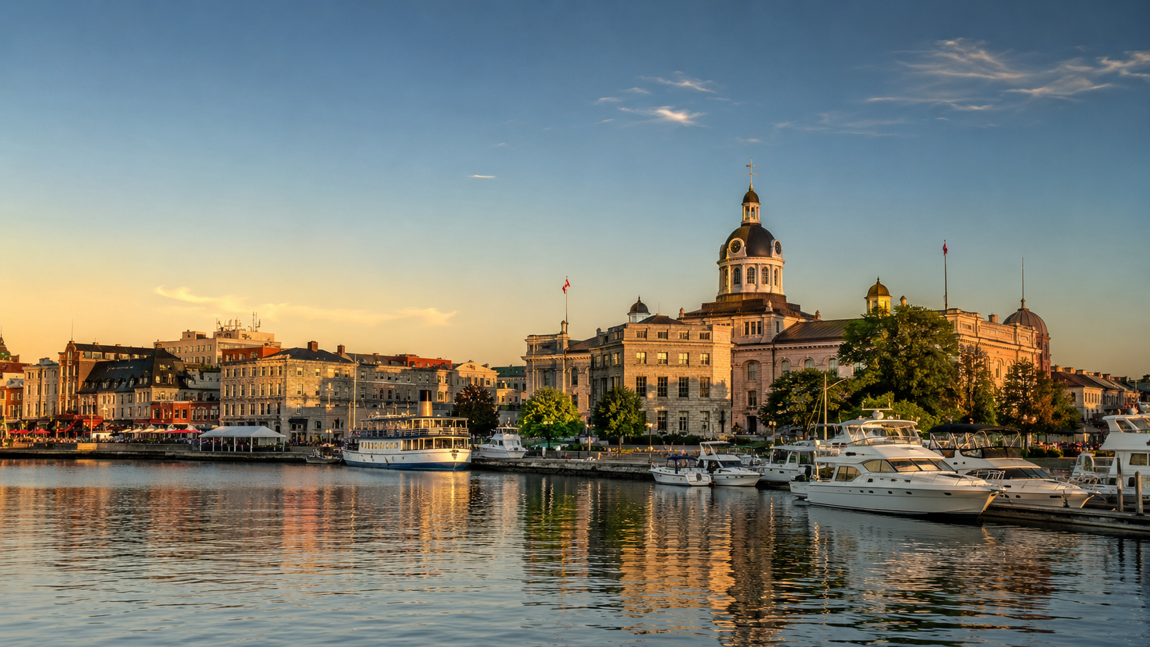 Kingston waterfront at golden hour with City Hall, marina boats, historic limestone buildings and Lake Ontario reflections.
