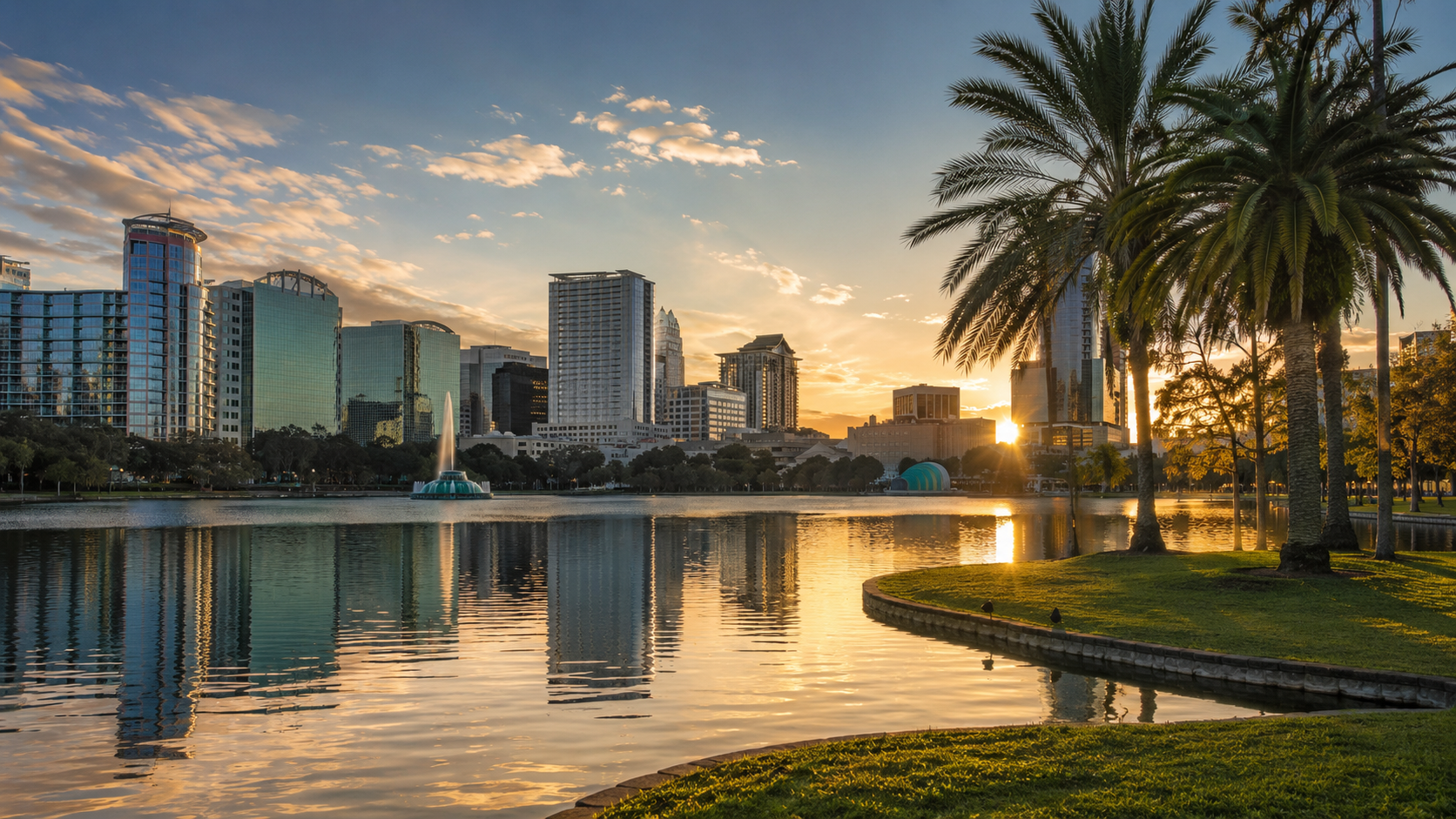 Orlando skyline at sunset with Lake Eola, palm trees, downtown buildings, fountain and water reflections in Florida.