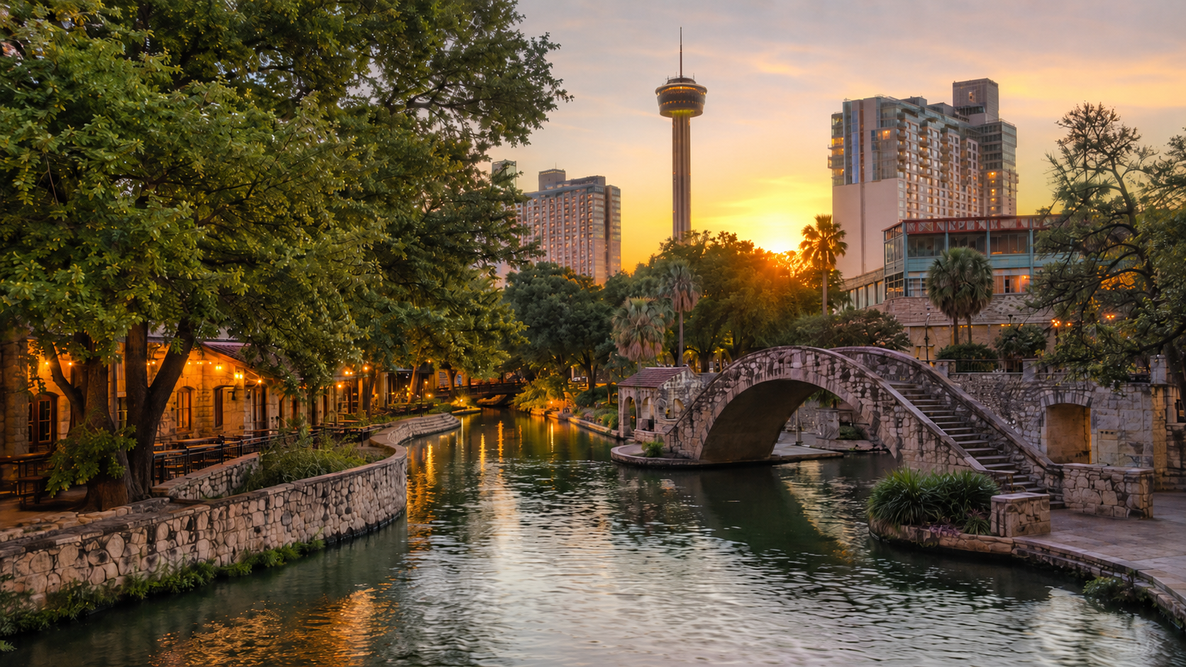 San Antonio River Walk at golden hour with stone bridge, canal reflections, downtown skyline and Tower of the Americas in Texas.